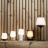 Een reeks draadloze tafellampen van sackit met warme verlichting op een houten plank tegen een verticale houten wand inclusief de Ambience Intelligent lamp