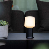 Draadloze tafellamp van sackit met zwarte voet en warme witte verlichting op een donkere tafel in een stijlvol interieur