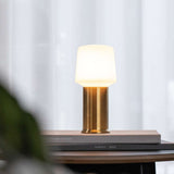 Draadloze tafellamp van sackit met warm wit licht en bronzen voet op gestapelde boeken in een stijlvol interieur