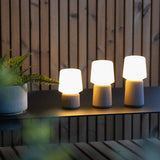Drie Ambience draadloze tafellampen van sackit met warme verlichting op een donker meubel tegen een houten wand te zien