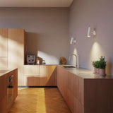 Twee witte sackit Expo Wall wandlampen verlichten een warme moderne keuken met houten kasten werkblad en visgraatvloer sfeervol en gericht