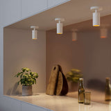 Drie witte cilindrische plafondlampen van sackit met warm licht boven een keukenplank met plant houten snijplanken en glazen flessen in een modern interieur