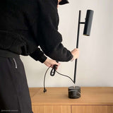 Persoon monteert een zwarte tafellamp met slanke staander en marmeren voet op een houten tafel in een modern interieur