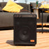 Draagbare zwarte Bluetoothspeaker van sackit met handvat op een houten tafel in een sfeervol interieur met bank en gele kussens