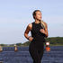 Vrouw jogt langs het water met sackit Active 200 oordopjes tijdens een buitentraining in zwarte sportkleding