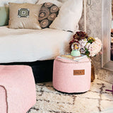 Roze ronde sackit Cobana Junior poef in een sfeervolle slaapkamer met bloemen op een zacht vloerkleed naast een bed en fauteuil