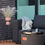 Donkergrijze modulaire loungesofa van sackit met zachte plaid in een stijlvolle Scandinavische buitenruimte naast een ronde salontafel en plantenstandaard