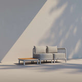 Teakhouten buitentafel van gepoedercoat aluminium naast een comfortabele loungesofa met kussens van sackit in een rustige buitenruimte