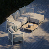 Outdoor salontafel met teakhouten blad en aluminium onderstel tussen een lichte loungesofa fauteuil en hocker op een houten terras