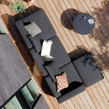 Donkergrijze modulaire loungesofa met losse pouf op een zonnig houten terras met zachte kussens en een ronde bijzettafel van sackit ontworpen in Denemarken