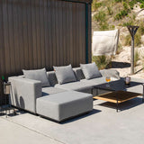Modulaire grijze buitenbank met losse poef en zachte kussens naast een zwarte salontafel, ontworpen voor comfortabel loungen in de tuin door sackit
