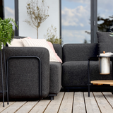 Donkergrijze modulaire loungesofa met armleuning van sackit op een houten terras met zachte kussens planten en een stijlvol bijzettafeltje in Scandinavische sfeer