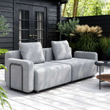 Modulaire lichtgrijze outdoor sofa met zachte kussens en armleuningen op een houten terras in een groene tuin ontworpen door sackit voor Scandinavisch buitenleven