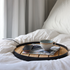 Ronde houten dienbladtafel met zwarte rand op een bed met koffiekopje smartphone en tijdschriften als stijlvolle setting voor sackit buitenmeubilair