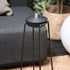 Zwarte metalen buitenstandaard met rond plateau en zilverkleurige houder naast een bank en ronde buitenlamp in een modern interieur
