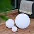 Drie witte ronde sackit Light 350 lampen op een houten terras naast een loungesofa met plaid voor sfeervolle buitenverlichting tijdens zomeravonden