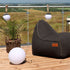 sackit Light 250 draadloze buitenlampen op een houten terras naast een donkere loungestoel en palmplant met weids uitzicht over het landschap
