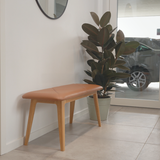 sackit houten bankje met cognackleurige leren zitting en slanke eiken poten in een modern interieur met een groene plant naast een glazen deur