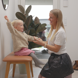 Kind speelt op een leren bank met houten poten terwijl een vrouw helpt in een licht Scandinavisch interieur van sackit