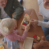 Kind speelt met houten speelgoed op een cognackleurige leren zitbank terwijl twee volwassenen toekijken in een warm Scandinavisch interieur