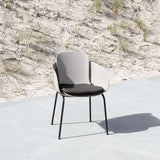 Patio stoel met donker zitkussen op een licht terras naast een duinlandschap met helmgras ontworpen voor comfortabel buiten zitten