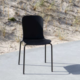 Zwarte outdoor stoel van sackit met ergonomische rugleuning op een betonnen terras naast duingras en zand. Ontworpen voor comfortabel buiten eten en ontspannen.