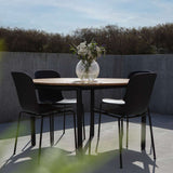 Zwarte buitenstoelen rond een houten tuintafel op een modern terras met betonnen muur en vaas met bloemen. sackit tuinmeubilair voor comfortabel buiten eten.