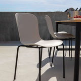 Twee lichtgrijze tuinstoelen van sackit met gebogen rugleuning en zwart metalen onderstel op een zonnig terras naast een houten buitentafel