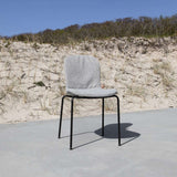 Grijze patio stoel van sackit met zachte bekleding en zwart metalen onderstel op een betonnen terras voor duinen en helmgras