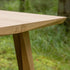 Detail van een eikenhouten eettafel met verfijnde gefacetteerde rand en schuin toelopende houten poot in een groene buitenomgeving
