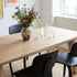 sackit eikenhouten eettafel in een lichte eetkamer met zwarte stoelen en een kleurrijke bloemenvaas op tafel