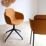 Twee cognackleurige leren eetkamerstoelen met afgeronde armleuningen en zwarte poten in een licht Scandinavisch interieur van sackit