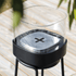Zwarte patio accessoirehouder van sackit met glazen windscherm en metalen deksel op drie poten op een houten terras