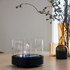 sackit bio lamp met levende vlam in een zwarte houder en glazen cilinder op een houten tafel in een sfeervol interieur met decoratieve takken