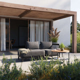 Donkergrijze modulaire loungesofa met open uiteinde op een zonnig terras met houten overkapping en salontafel van sackit ontworpen voor buitengebruik