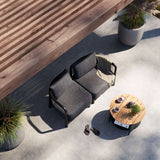 Donkergrijze modulaire loungesofa voor buiten met twee zitplaatsen van sackit in een zonnige tuin met ronde houten tafel en planten