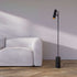 Minimalistische zwarte vloerlamp van sackit met slanke aluminium staander en marmeren voet naast een lichte bank in een modern interieur