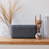 Donkergrijze draadloze Move 150 speaker van sackit op een houten plank met droogbloemen en decoratieve objecten in een Scandinavisch interieur