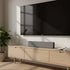Grijze sackit Wave Soundbar onder een zwarte televisie op een licht houten tv meubel in een modern interieur met een groene kamerplant