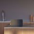 Move 50 Care luidspreker van sackit op een houten keukenblad in een modern interieur met donker textiel en warme houtaccenten