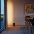 Slanke zwarte vloerlamp van sackit met subtiel verticaal licht langs de wand en een marmeren voet in een warm modern interieur met houten vloer en eettafel