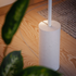 Witte Expo 185 vloerlamp van sackit met cilindrische marmeren voet en slank armatuur op een houten vloer tussen groene planten