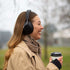 Vrouw met een zwarte over ear koptelefoon van sackit geniet buiten van muziek met een warme koffiebeker in de hand en een sjaal om haar nek