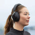 Vrouw met zwarte Touch 310 over ear hoofdtelefoon van sackit tijdens een wandeling buiten met een comfortabel ontwerp en actieve ruisonderdrukking