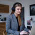 Vrouw werkt aan een laptop terwijl ze een zwarte sackit Touch 400 over-ear hoofdtelefoon draagt in een modern interieur