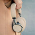 Beige Touch 400 over ear hoofdtelefoon van sackit met zachte oorkussens wordt naast een beige jas vastgehouden