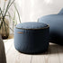 Donkerblauwe ronde Cura poef van sackit met decoratieve stikrand op een houten vloer naast een blauwe zitzak en kamerplant