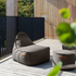 Donkergrijze outdoor zitzak met bijpassende poef op een houten terras in de zon met een zwarte balustrade en groene tuin op de achtergrond
