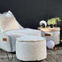Lichtgrijze outdoor poef van sackit naast een bijpassende lounge fauteuil op een terras met houten vloer en ronde bijzettafel ingericht voor ontspannen buiten zitten