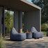 Grijze Cobana poef tussen twee comfortabele loungestoelen op een houten terras bij een modern huis van sackit
